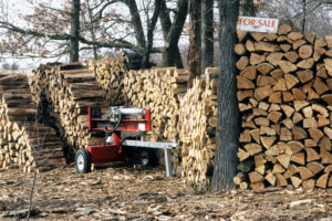 A large stack of firewood with a sign next to it that says "For sale."