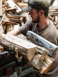 Man loads firewood into arms from back of truck.