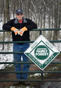 Forest landowner Jim Schiller at the entrance of his property with a Tree Farm sign hanging on the gate.