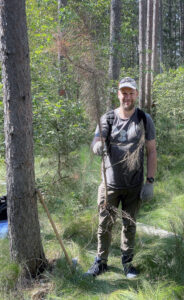 A worker in the woods, holding a young tree to be planted.