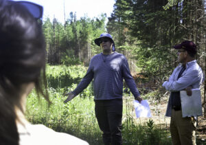 A worker speaks with colleagues in a forested area.